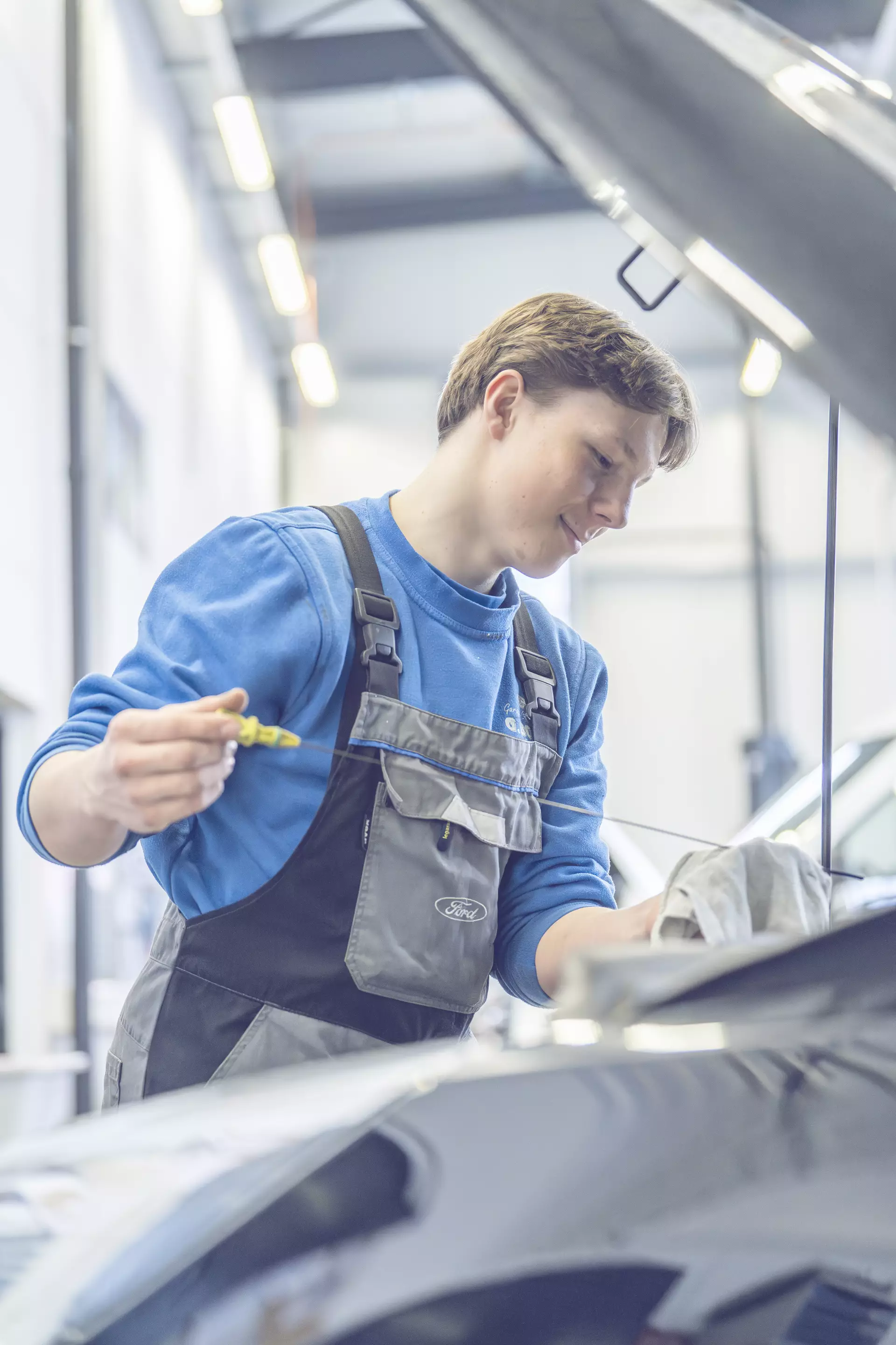 Apprenti mécanicien prenant la mesure de l'huile sous un capot de voiture