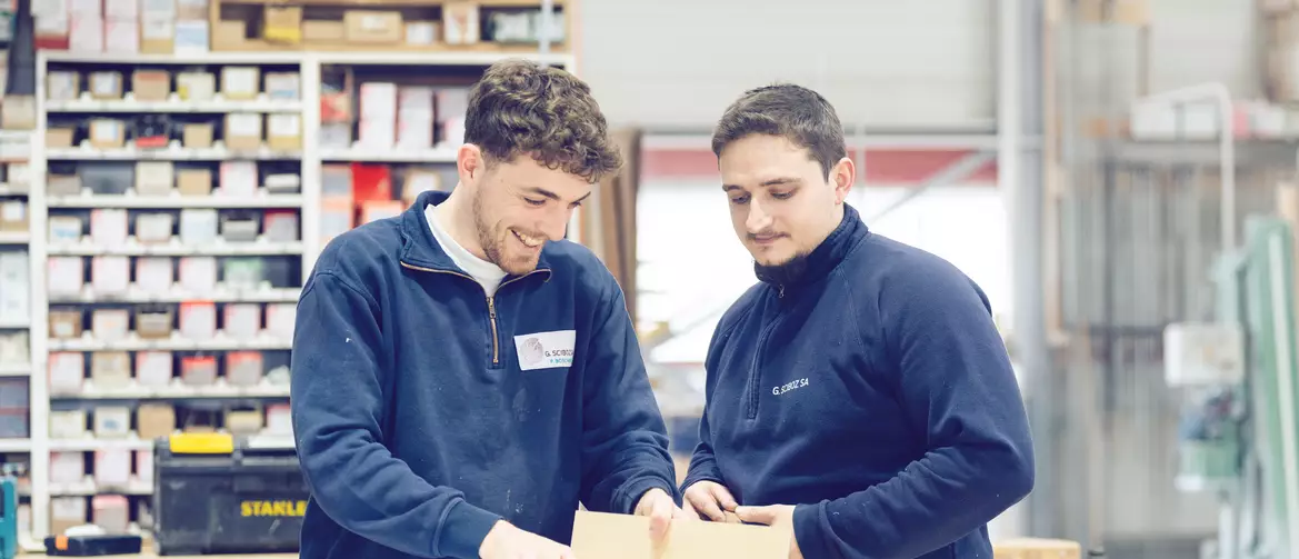 Apprenti et formateur charpentier en souriant tout en échangeant autour d'un projet