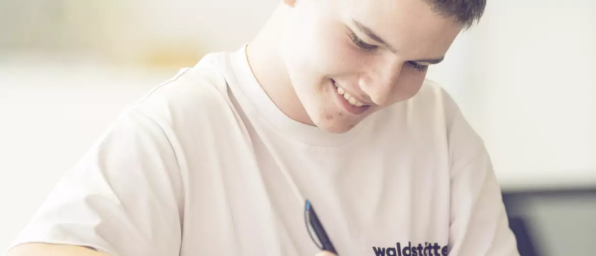 Apprenti dessinateur en batiment écrivant accoudé à une table haute